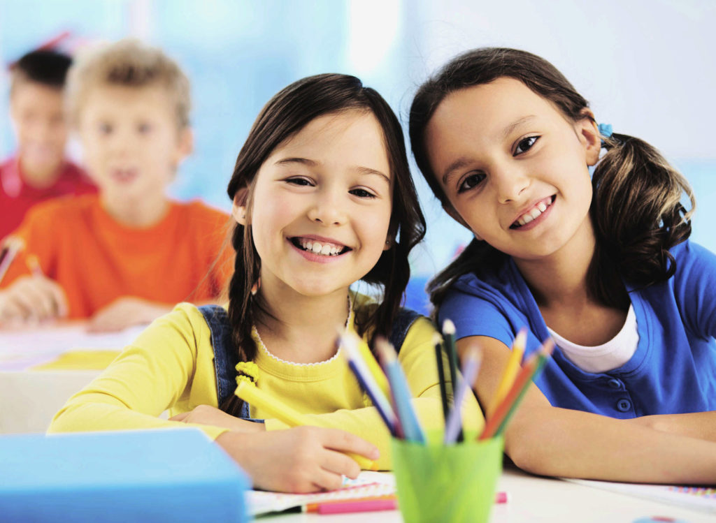 Two elementary school girls in class smile at camera