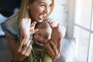Mom and baby playing and laughing together but holding feet.