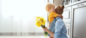 Toddler boy hugging mom while she hold yellow flower