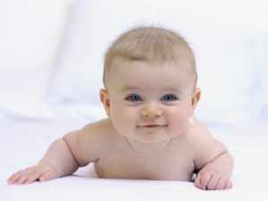 Smiling baby in diaper laying on stomach while looking up at camera