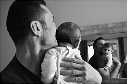 Black and white picture of dad holding baby and looking into a mirror