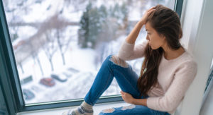 Depressed women staring out window over winter scene